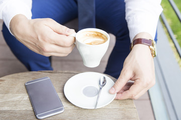 Close up of business man hands with cup of coffee and phone