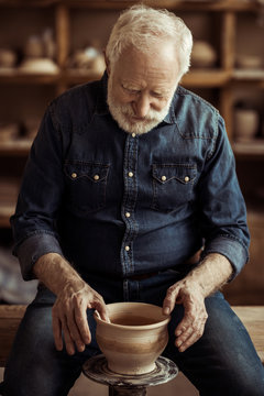 Senior Potter Making Pottery On A Wheel At Workshop