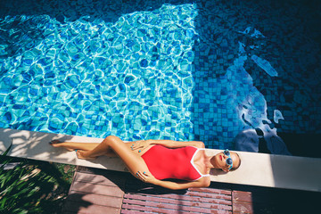 Enjoying suntan and vacation. Colorful portrait of pretty young woman in red swimsuit lying near...
