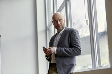 Fototapeta premium Bald Businessman Standing With a Mobile in His Hands