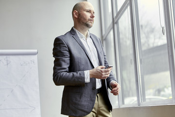 Fototapeta premium Bald Businessman Standing With a Mobile in His Hand