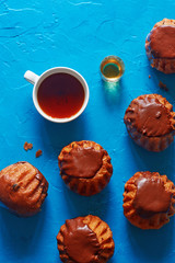 Vertical top view of chocolate rum baba and cup of black tea on blue concrete background.