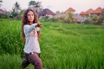 Young woman is stretching in asana pose standing on green grass. Concept of yoga and fitness outdoors.