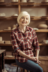 Front view of senior woman sitting on chair against shelves with pottery goods