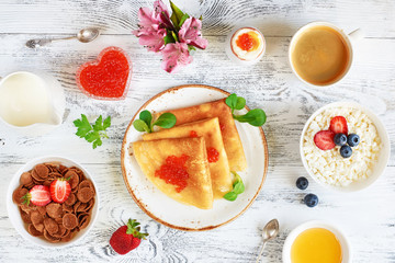 Top view of assorted russian breakfast on white wooden table. Pancakes with caviar, cottage cheese, honey, cereal, boiled egg, coffee and milk. 