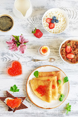 Traditional russian breakfast on white table. Top view of crepes with caviar, rye bread, boiled egg, cottage cheese and cereal. 