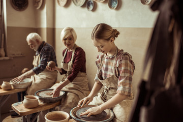 Grandmother and grandfather with granddaughter making pottery at workshop