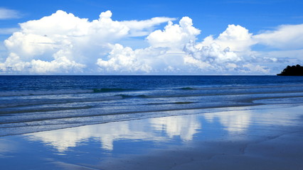 weiße Wolken spiegeln sich am blauen Meersstrand