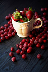 Bowl of juicy strawberries on a dark wood background.On top of Rossana berry. Cherry, strawberry, cranberry
