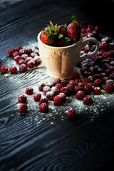 Bowl of juicy strawberries on a dark wood background.On top of Rossana berry. Cherry, strawberry, cranberry