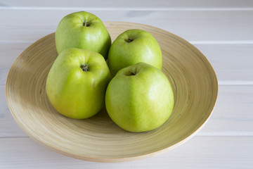 Four beautiful big juicy green apples on a wood plate