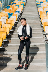 Obraz premium tired asian sportswoman with sport bottle and towel on stadium seats