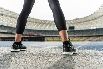 Close-up partial view of young sportswoman in sneakers standing on running track stadium