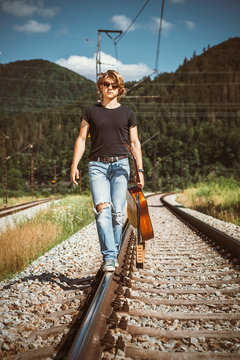 Young man with guitar walks on railways