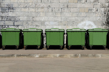 Green garbage containers standing in a row in the backyard of an industrial building. - 148022038