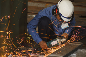 Worker with the face guard and electric wheel grinding on steel plate in factory. Heavy work concept.