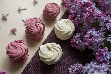 Pink and white marshmallows on a table with lilac flowers. Sweets and food in the kitchen.