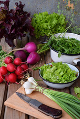 Fresh spring vegetables: radish, green and purple lettuce, onions, arugula on a wooden background. Preparation of food, salad. Healthy food.