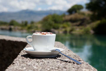 Чашка кофе на фоне реки и гор.