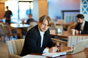 Middle-aged entrepreneur focused on work while sitting in spacious cafe, modern laptop, documents and notebook located on table