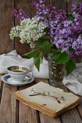 Romantic composition of  bouquet white and purple lilacs, cupcakes with curd cream, cups coffee, old book on wooden background. Space for text