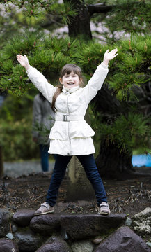 A sweet happy little girl laughs, raising his hands against the background of Japanese pine in Kyoto, Japan