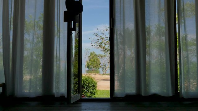 Open balcony door with white curtains and beach view