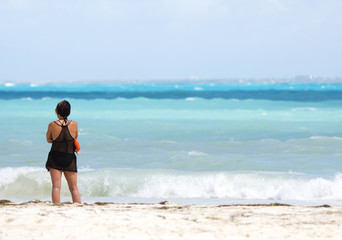 Lonely woman looking at the sea. She is standing on the beach. The woman is composed to the left.