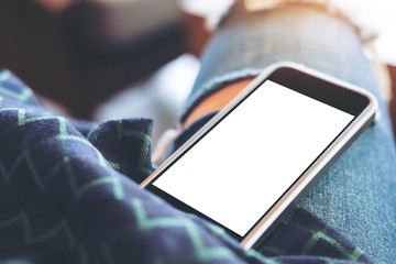 Mockup image of black mobile phone with blank white screen on woman's thigh in cafe