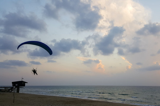 Silhouette of a male paraglider on a paraplan against a background of a sunset in the sky and clouds hovering over the sea. Concept: freedom, loneliness, hobby, sport.