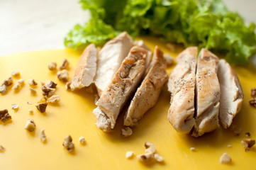 Ruddy chicken breasts with leaf salad and crushed walnut on yellow cutting board.