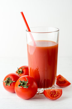 Tomato juice in glass and fresh tomatoes on white wooden table.