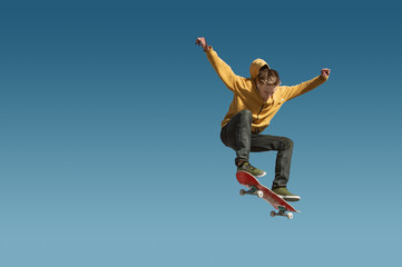 Obraz na płótnie Canvas A teenager skateboarder does an ollie trick on background of blue sky gradient