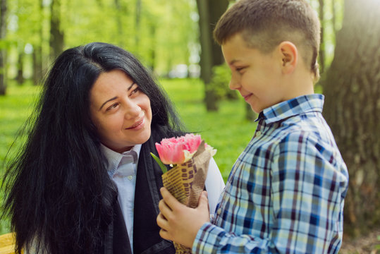 The son gives his mother a fresh bouquet of tulips flowers on a bench in the park. Family photo session.