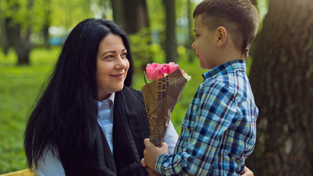 The son gives his mother a fresh bouquet of tulips flowers on a bench in the park. Family photo session.
