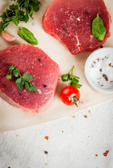 Raw beef, steak, cutlet. Meat, a source of protein. On a cutting board, on a white stone table. With spices, herbs and tomatoes for cooking. Copy space