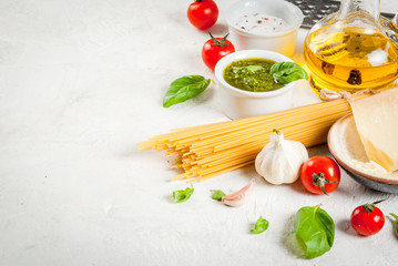 Ingredients for the preparation of Italian pasta with pesto sauce: spaghetti, olive oil, tomatoes, basil, parmesan cheese, pesto sauce, basil, garlic. On a white stone table. Copy space