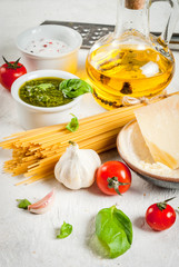 Ingredients for the preparation of Italian pasta with pesto sauce: spaghetti, olive oil, tomatoes, basil, parmesan cheese, pesto sauce, basil, garlic. On a white stone table. Copy space