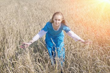Naklejka na ściany i meble The beautiful woman in a blue long dress in the field of ripe cereals..