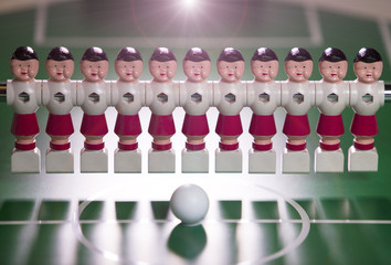 toy football players stand in the field in a row and a ball in the center..