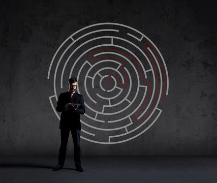 Businessman with computer tablet standing over labyrinth background. Business, strategy, concept.