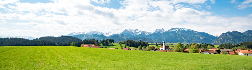 Fototapeta na wymiar Allgäulandschaft mit Dorf und Alpen im Hintergrund, Banner