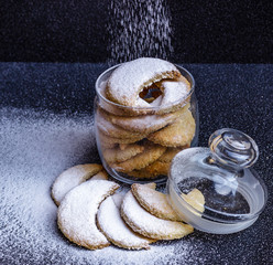 Homemade half-moon shaped cookies in a glass jar with sprinkled powdered sugar