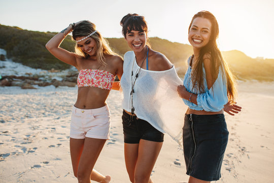 Three young women laughing on beach at sunset