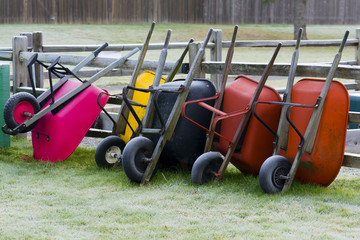 Wheel barrows put away leaning against fence outside of community garden.