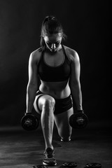 Woman bodybuilder lifting dumbbell isolated over black background, Black and white.