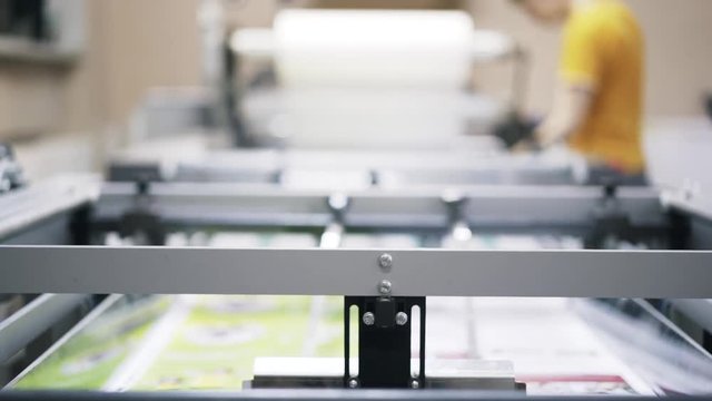 Front view of an industrial printer working making posters. Tilt down slow motion close up shot