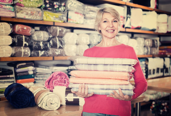 Smiling senior seller is showing wide assortment of bed linen
