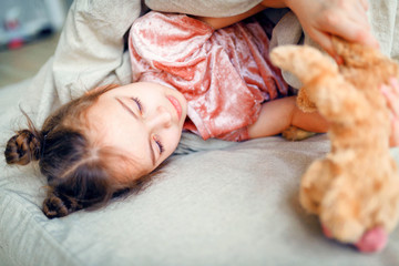 child little girl sleeps in the bed with a toy teddy bear