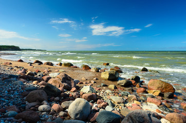 Sunny day with blue sky on the beach with many stones. Waves on the background.